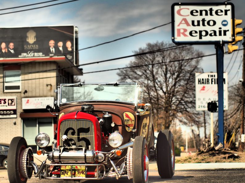 Carburetors - a red car driving down a street next to a tall building