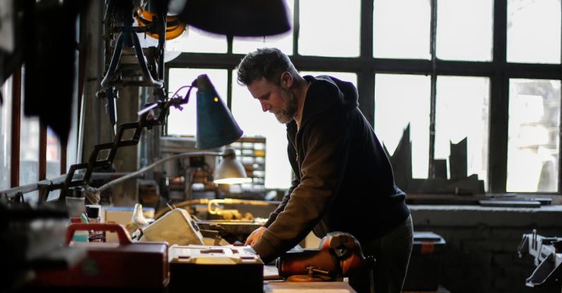 Check Engine Light - Side view of serious adult bearded male mechanic in workwear standing near workbench and working with details of engine in light of lamp in garage