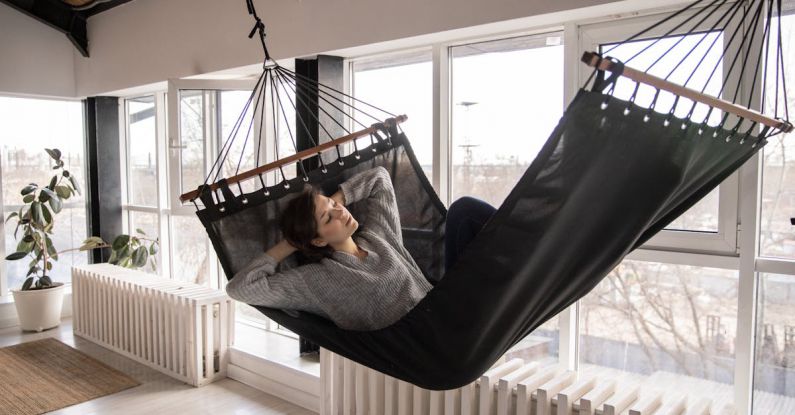 Radiator - Young female in casual wear lying in comfortable hammock with eyes closed leaned on hands while sleeping in apartment near window and radiators with potted plant