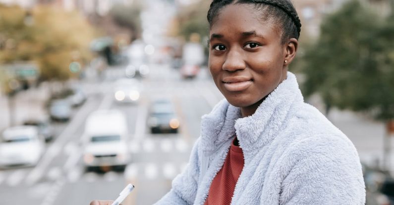 Car Organizers - Delighted young African American female student looking at camera while standing on footbridge over road and taking notes in notepad