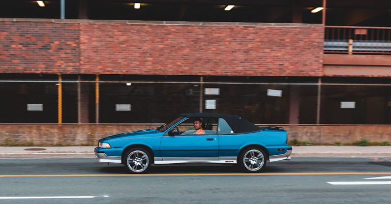 Convertible Top - Side view of old timer blue cabriolet riding on highway near construction with brick wall on street in city outside
