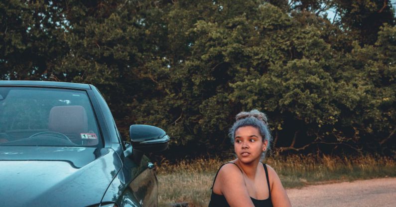 Wheel Size - Full body of young plump ethnic female sitting on hunkers near shining expensive car parked against trees
